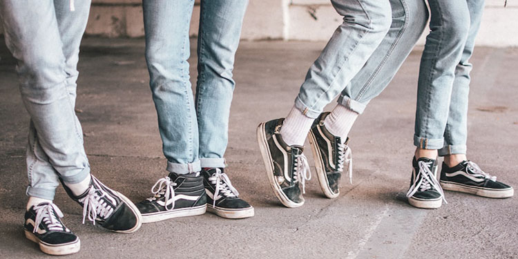 Groupe de jeunes portant des jeans clairs slim roulottés et des baskets noires rétro de type Vans, illustrant un style décontracté emblématique des années 80 dans un décor urbain.