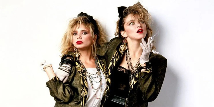 Deux femmes arborant un look inspiré de Madonna dans les années 80, avec vestes oversize, cheveux ébouriffés, gants en dentelle, bijoux superposés, maquillage prononcé et attitude rebelle typique de la mode new wave.
