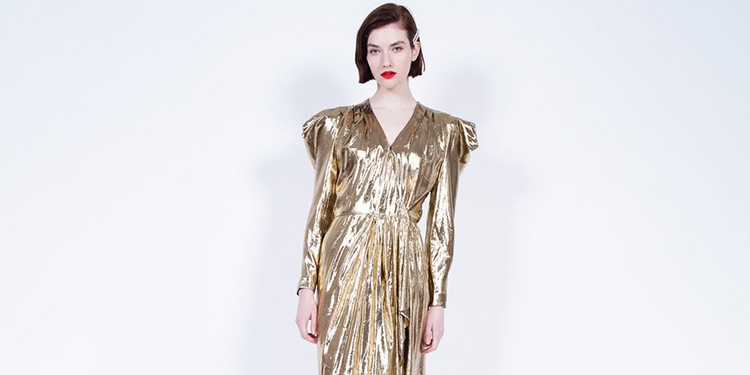 Femme portant une robe dorée métallisée au style typique des années 80, avec manches longues, épaules structurées et coupe drapée élégante pour un look glamour vintage.