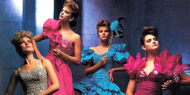 Quatre femmes en robes de soirée typiques des années 80 avec volants, bustiers brillants, épaules exagérées et couleurs intenses comme le rose fuchsia, le bleu vif et l’argenté, dans une mise en scène glamour et théâtrale.