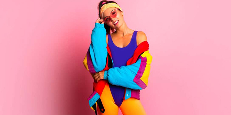Tenue fitness années 80 femme – Justaucorps violet, veste colorblock fluo, leggings orange et bandeau rétro sur fond rose